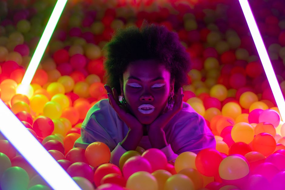 Artistic neon-lit portrait of a woman in a colorful ball pit with a futuristic feel.
