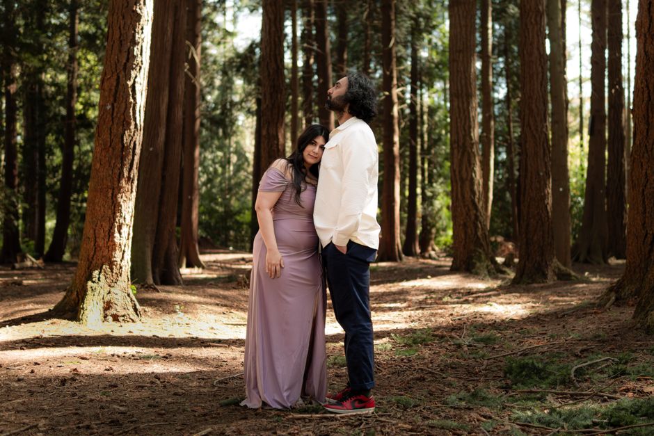 A couple lovingly embraces amidst tall trees in a serene forest setting.