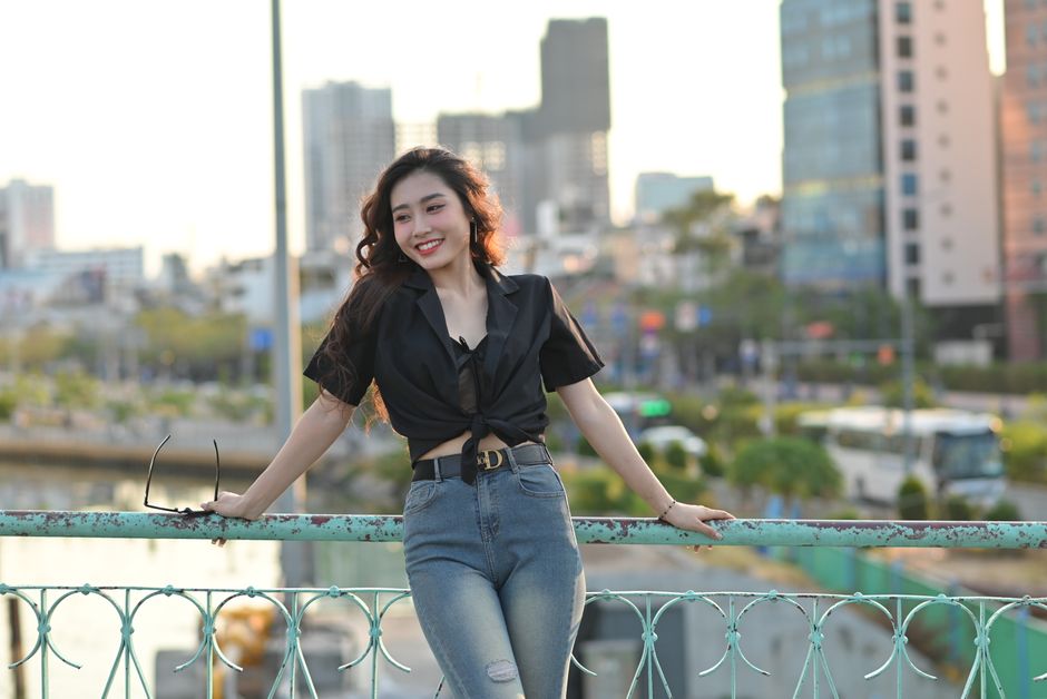 Stylish woman poses on a city bridge with a vibrant urban backdrop.