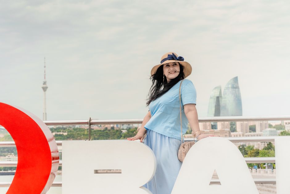 A woman in blue stands near Baku's Flame Towers in Azerbaijan, smiling warmly.