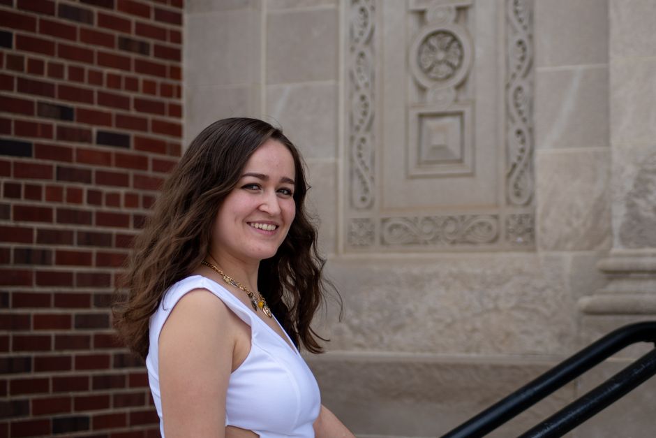 Smiling young woman in a white dress outside a historic stone building.