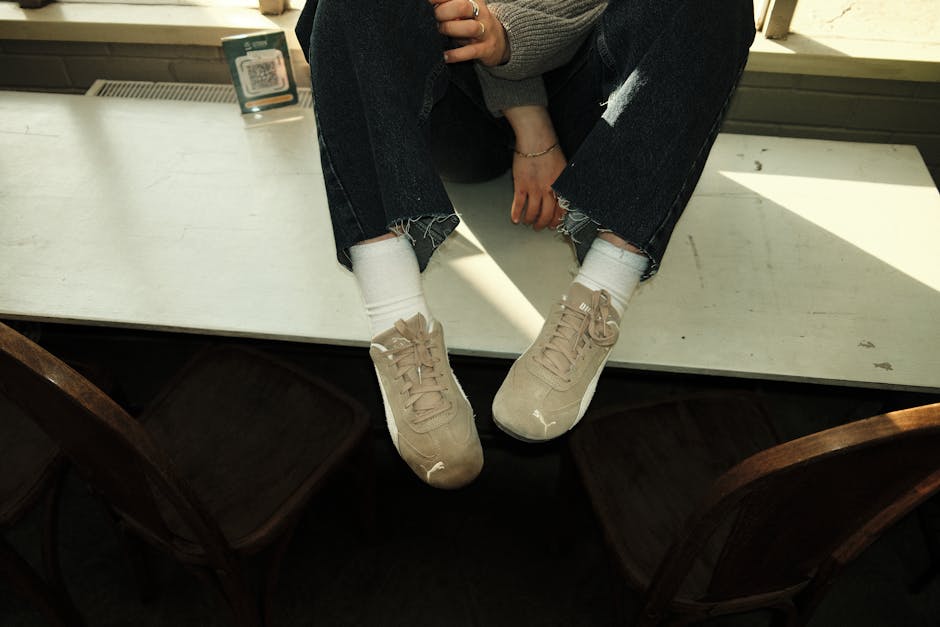 A casual scene with a person in sneakers and jeans sitting on a table in a softly lit room.