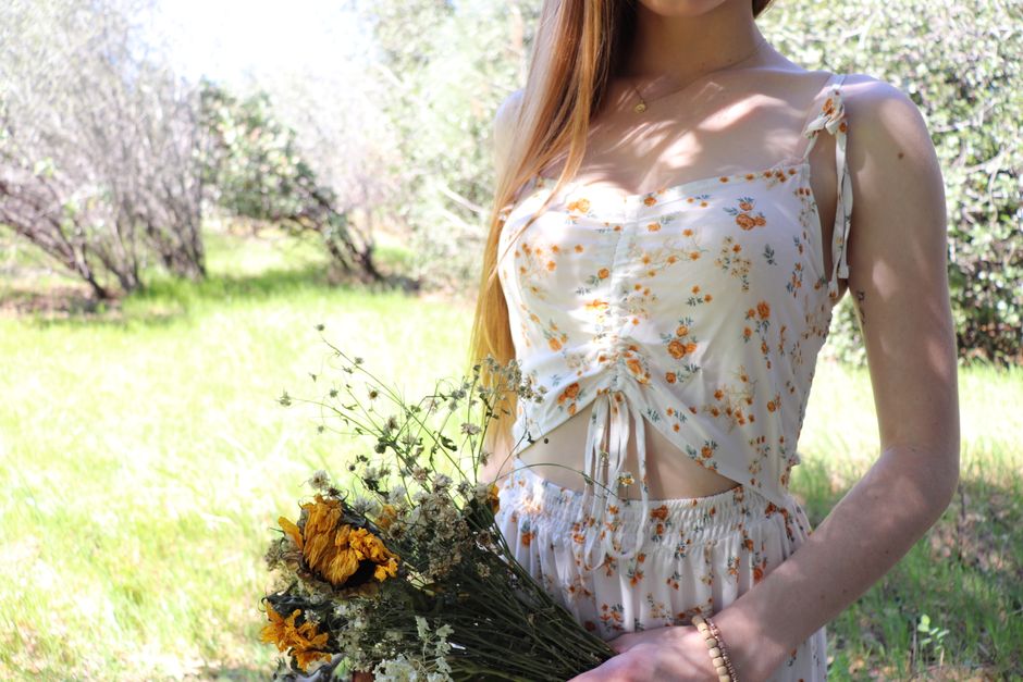 A woman in a stylish sundress holding wildflowers in a lush summer setting.