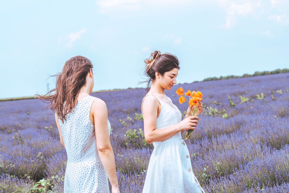 Two women enjoying a day in a lavender field, holding vibrant orange flowers.