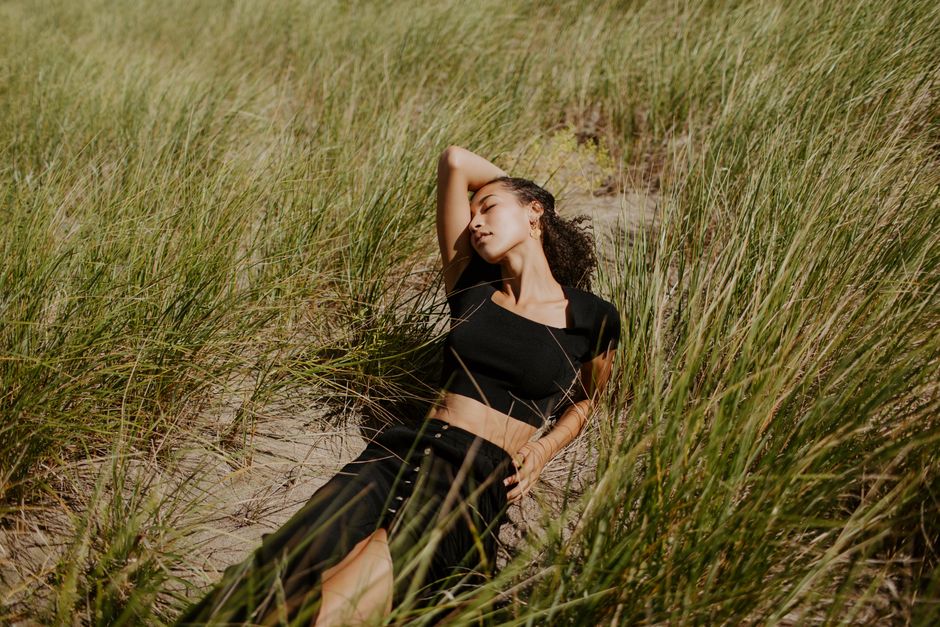 Woman lying with eyes closed in sunlit grassy field, displaying tranquility.