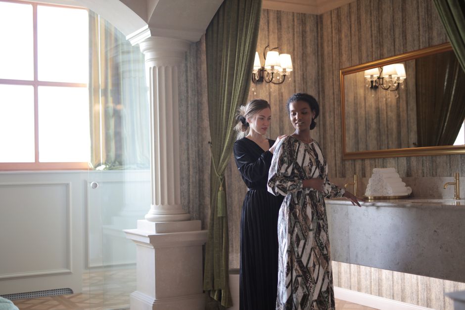 Two women in elegant dresses interacting in a stylish and luxurious restroom setting.