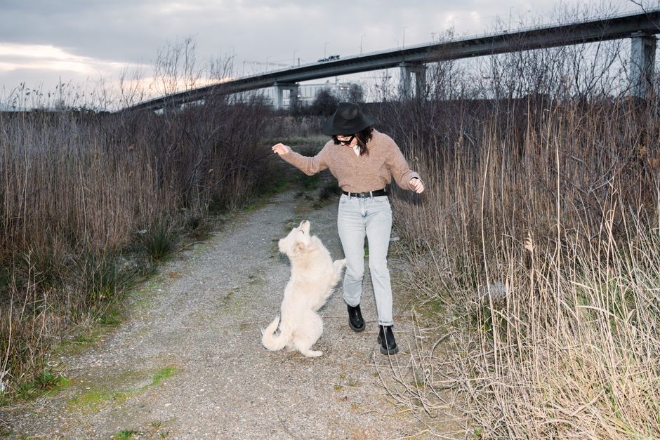 Young woman playing with her dog on a path under a bridge, enjoying outdoor time.