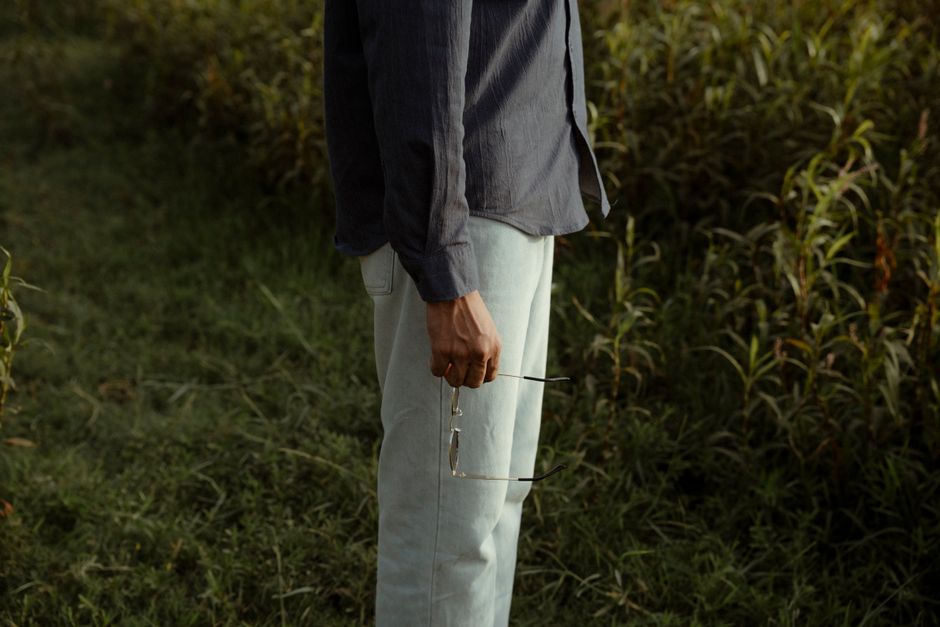 A person in casual attire holding sunglasses outdoors in a grassy field.