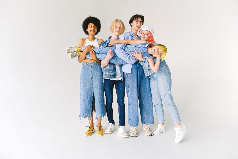 Full body of multiethnic teenagers and schoolchild in casual denim outfit standing in studio and holding kid on hands on white background