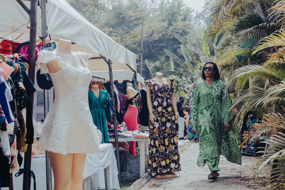A woman in a green dress strolls through an outdoor clothing market in Abuja, Nigeria.
