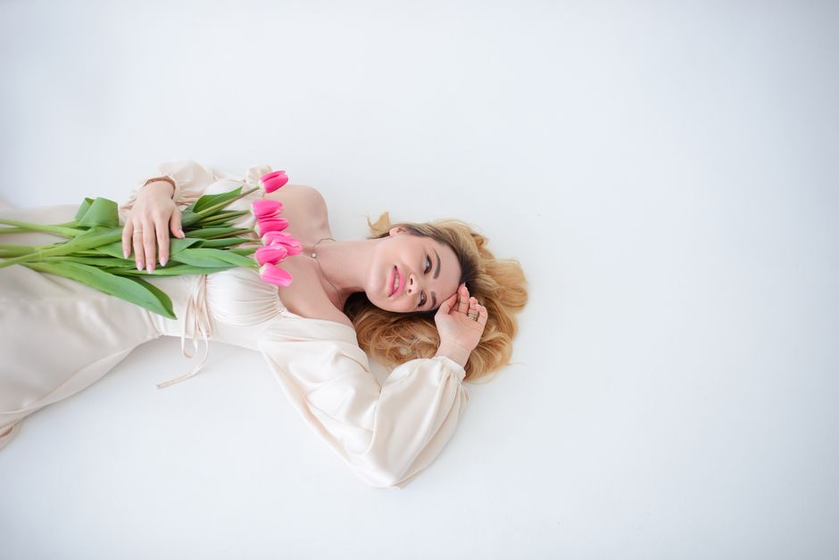 Relaxed woman lying with a bouquet of pink tulips on a minimalist white background. Spring vibes.