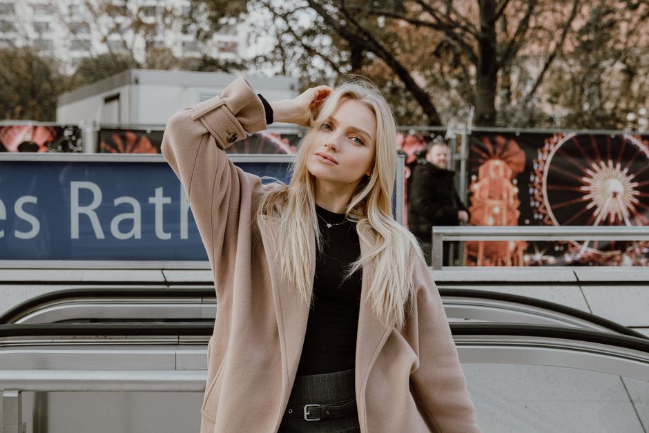Fashionable woman in a coat poses confidently outdoors, emphasizing style.