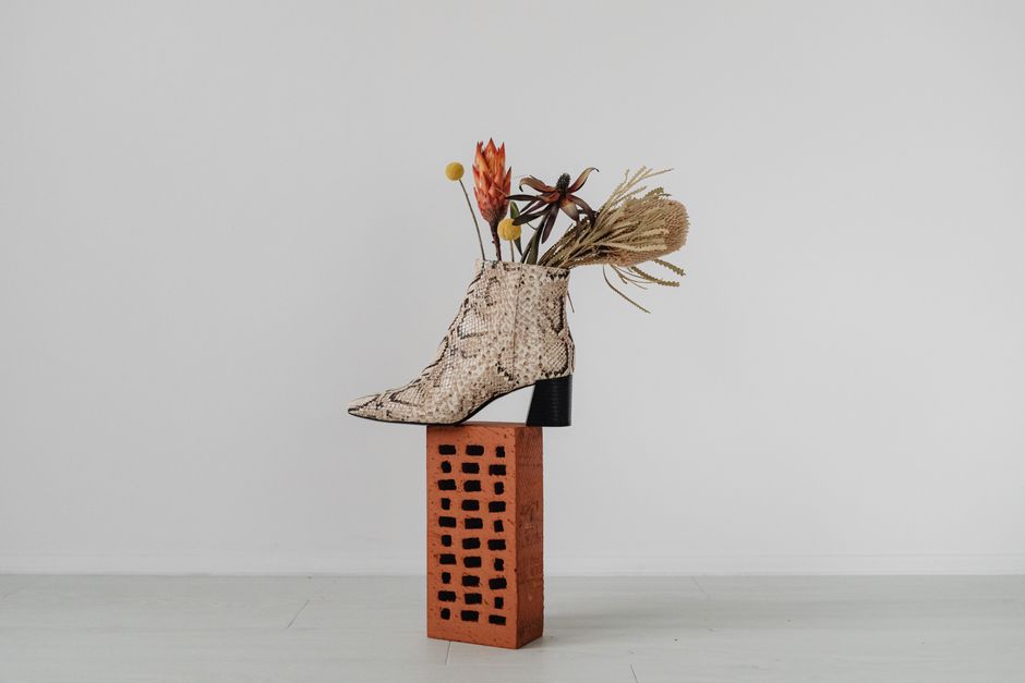 Artistic floral arrangement in a snake print boot on a brick for modern decor inspiration.