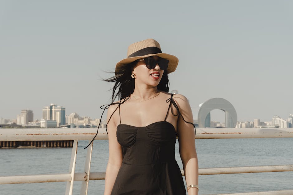 A fashionable woman in sunglasses and hat enjoying a sunny day by the Baku waterfront.