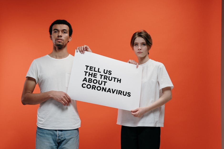 Two people holding a 'Tell Us The Truth About Coronavirus' sign against a vibrant orange background.