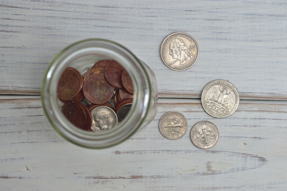 Top view of a jar filled with coins placed on a wooden table, depicting savings.
