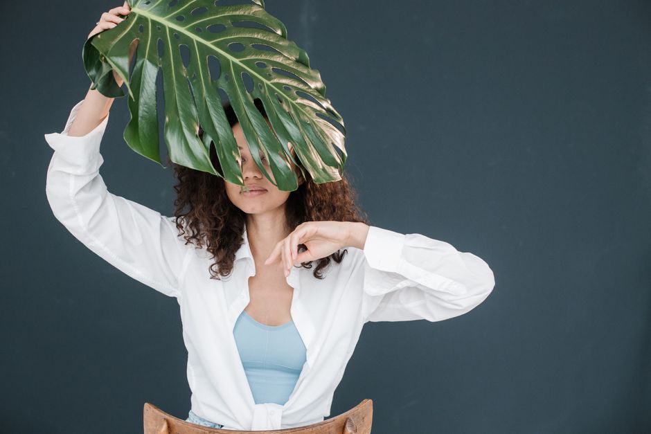 Creative indoor portrait of a woman partially hidden by a monstera leaf, highlighting minimalist fashion.