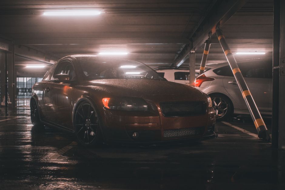Dark urban parking garage featuring a sleek wet sedan under dim lighting.