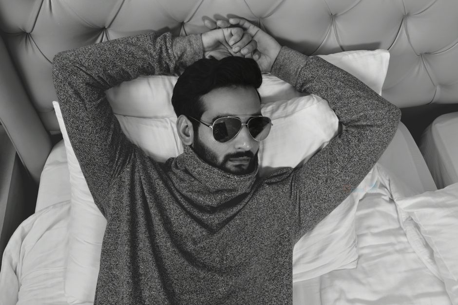 Stylish male model lying on bed wearing sunglasses in a monochrome room.