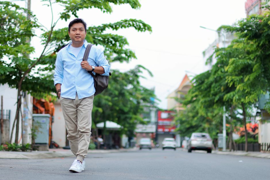 Man in casual attire walking confidently on a sunny city street.