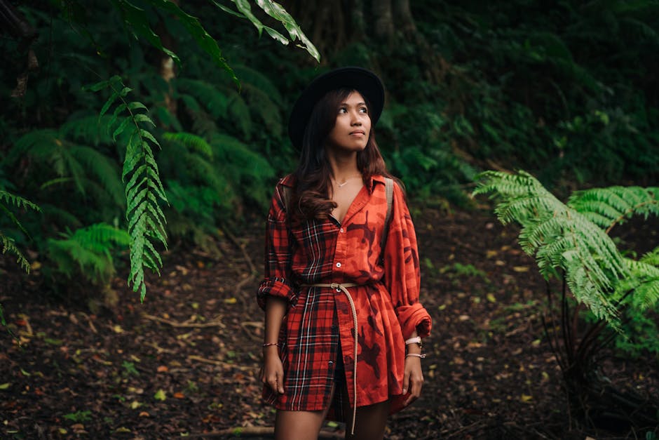 A woman in a red dress and hat explores a vibrant green forest, surrounded by lush foliage.