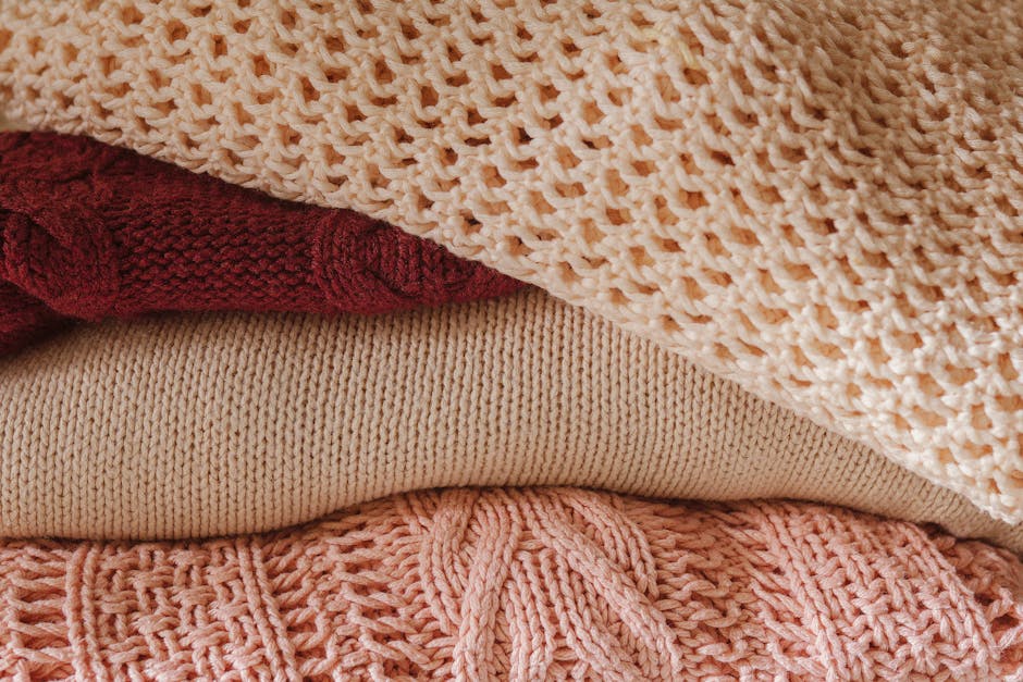 A close-up view of a cozy stack of knitted sweaters in warm shades, emphasizing texture and comfort.