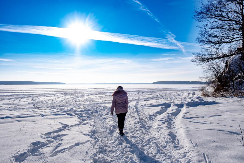 A person walking on a snow-covered field under a clear blue sky in Lithuania during winter.
