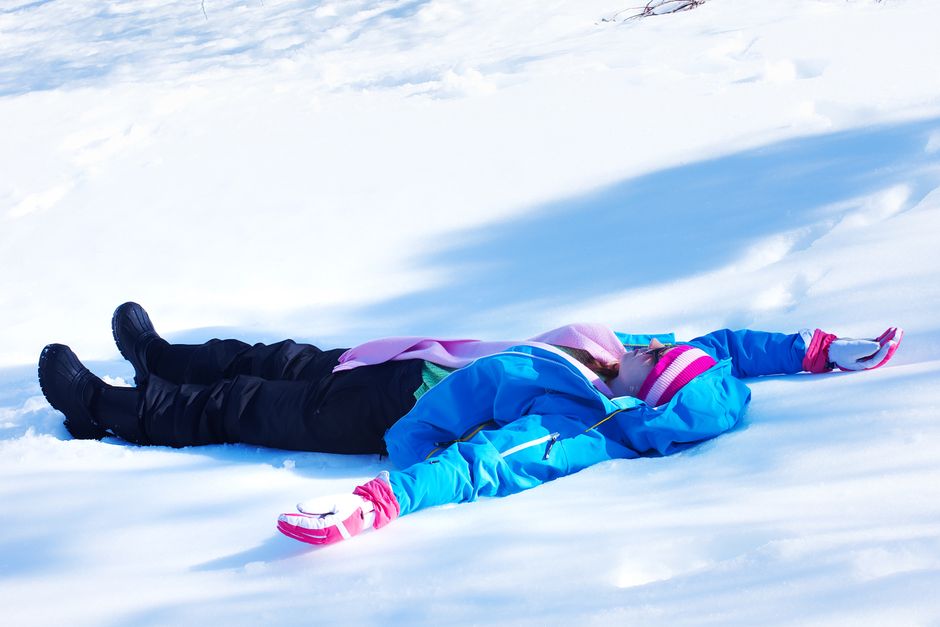 Child lying on snow making snow angels in winter clothing. Fun outdoor activity capturing a joyful moment.