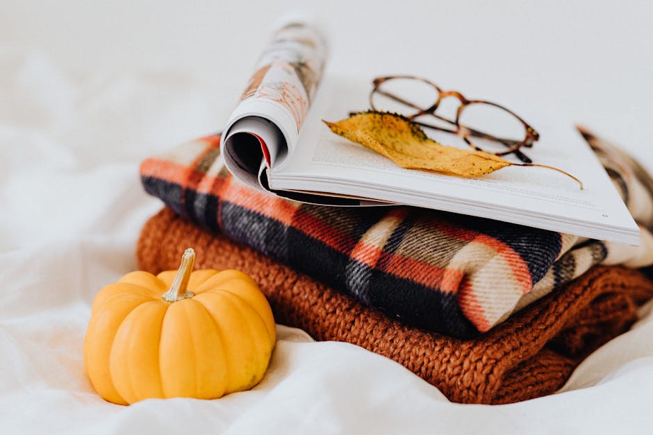 A warm, cozy still life featuring a plaid blanket, small pumpkin, and reading glasses on an open magazine.