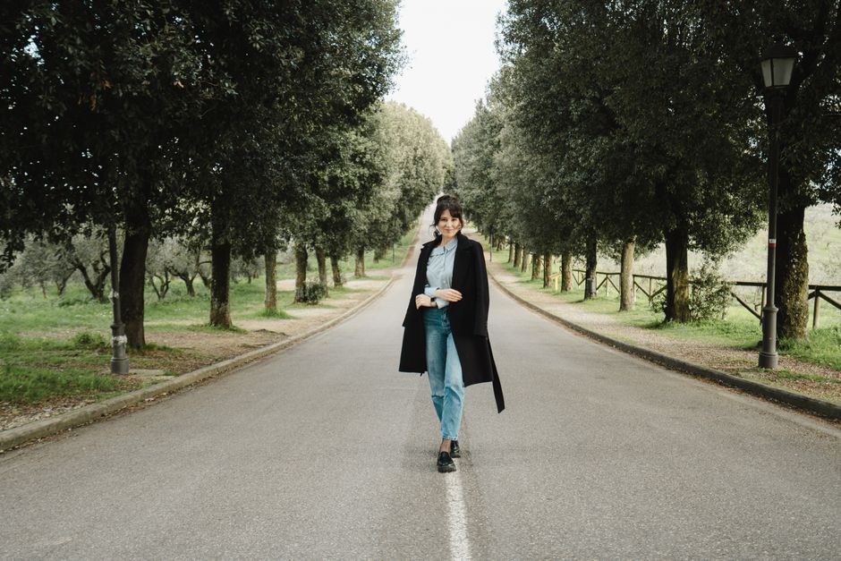 Stylish woman walking on a beautiful tree-lined road in the Tuscan countryside.