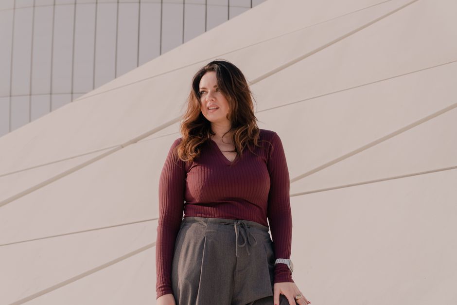 A woman stands confidently in front of a modern, abstract wall, enjoying a sunny day.