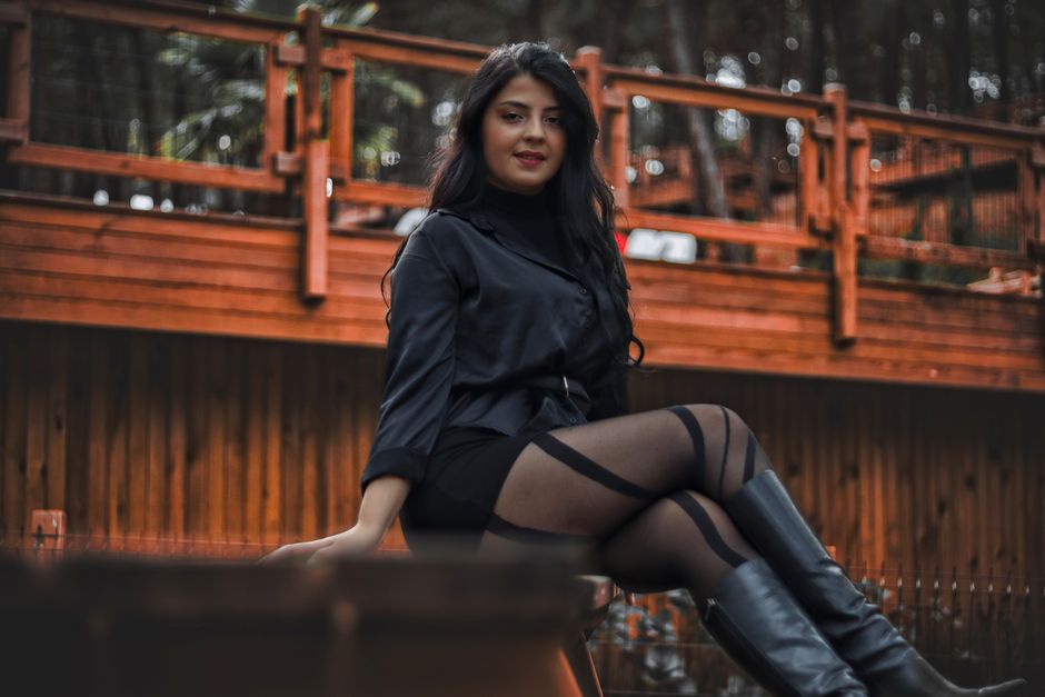A stylish woman sits outdoors, showcasing a chic outfit with boots. Perfect for fashion photography.