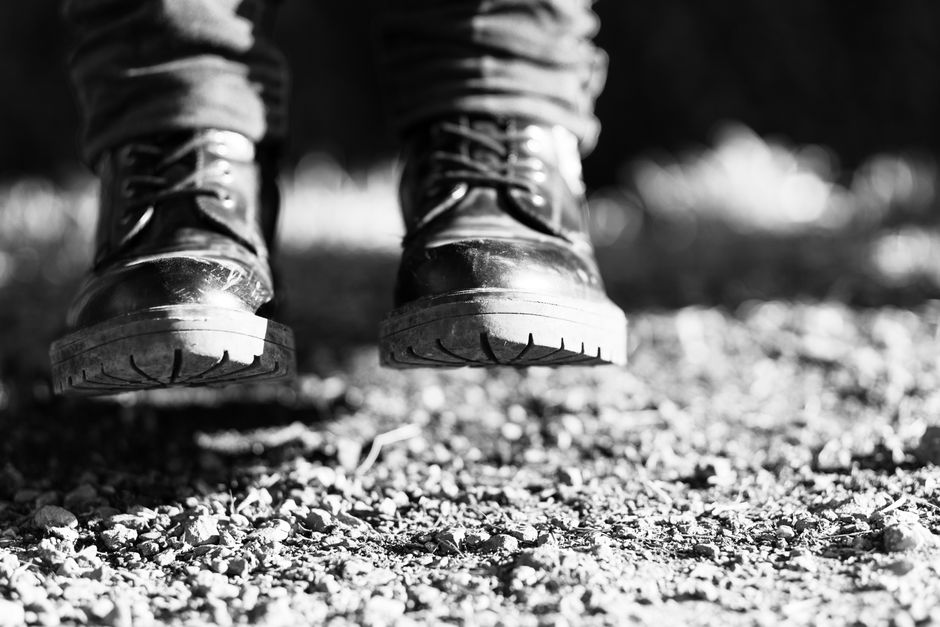 Close-up black and white shot of boots on a gravel surface, emphasizing texture.